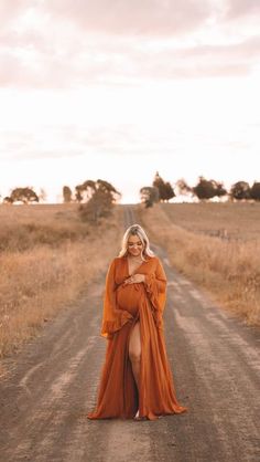 a woman in an orange dress standing on a dirt road with her arms around her waist