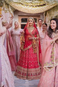 a woman in a red and gold bridal gown standing next to other brides