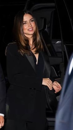 a woman in a black suit is standing next to a car