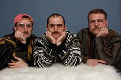 three men sitting next to each other in front of a white fur covered floor with their hands on their chins