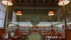 an empty library filled with lots of books and chairs next to tall lamps on the ceiling