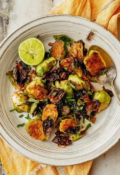 a white bowl filled with brussel sprouts and lemon wedges