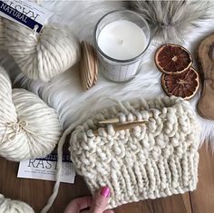 a woman's hand is holding a white knitted purse next to some oranges