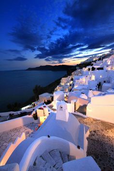 white buildings are lit up at night by the water's edge, with blue sky and clouds in the background