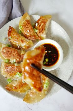 some food is on a white plate with chopsticks and sauce in the bowl