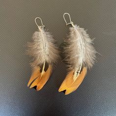 two pairs of earrings with feathers hanging from hooks on a table top, one is yellow and the other is brown