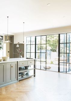 a large kitchen with wooden floors and gray cabinets, an island in the middle is surrounded by glass doors