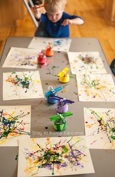 a young boy painting on paper with paintbrushes and watercolors in front of him