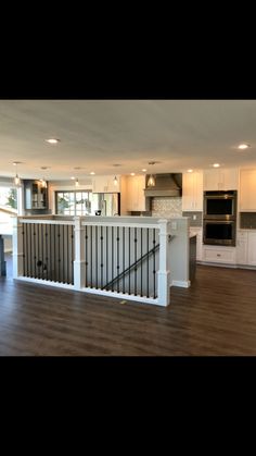 an empty kitchen and living room in a house with hardwood floors, white cabinets, and stainless steel railings