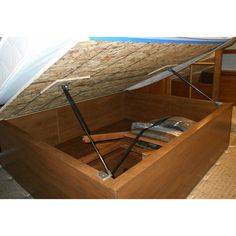 an open wooden box filled with items on top of a carpeted floor next to a bed