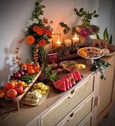 an assortment of fruits and vegetables on a buffet table with lit candles in the background