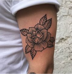 a black and white rose tattoo on the left upper half of the arm, with leaves around it