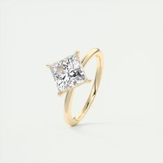 a yellow gold ring with a princess cut diamond in the center, on a white background