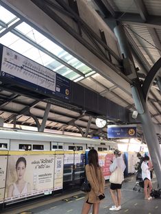 a woman standing in front of a train at the station with her back to the camera