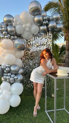 a woman sitting at a table in front of a bunch of silver and white balloons