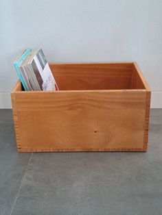 a wooden box with magazines in it sitting on the floor next to a white wall