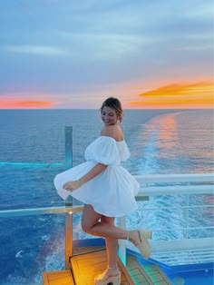 a woman posing on the deck of a cruise ship at sunset with her legs in the air