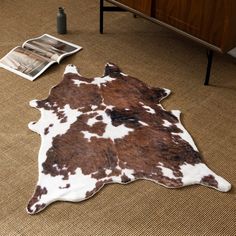 a brown and white cowhide rug sitting on top of a floor next to a magazine