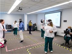 several people in scrub suits and masks are standing near a projector screen while others watch