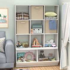 a white book shelf filled with lots of books next to a blue chair and window