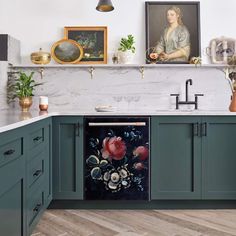 a kitchen with green cabinets and paintings on the wall