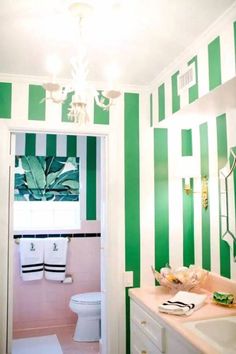 a bathroom with green and white stripes painted on the walls, sink, toilet and chandelier