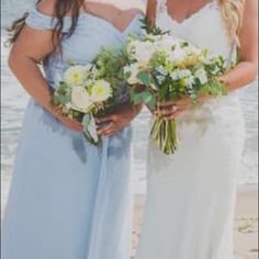 two women standing next to each other on a beach with flowers in their hands and one holding a bouquet