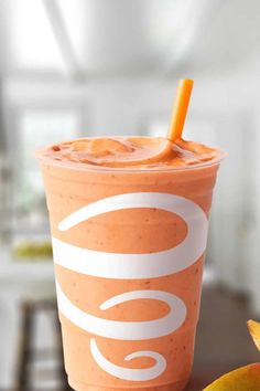 an orange smoothie in a plastic cup with a straw sticking out of the top