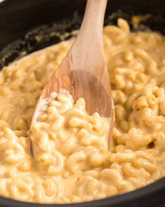 macaroni and cheese being stirred with a wooden spoon in a slow cooker