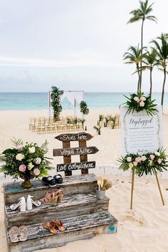 a wooden sign sitting on top of a sandy beach next to the ocean and palm trees