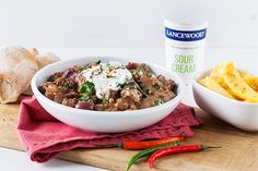 a wooden cutting board topped with a bowl of food next to a container of sour cream