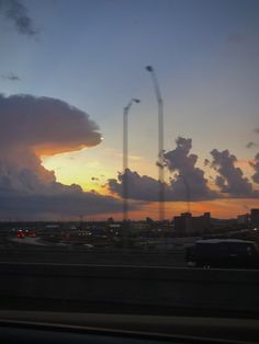 the sun is setting behind some clouds in the sky over a cityscape with cars driving on it