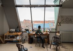 a person sitting at a table with a guitar in front of a large window overlooking the city