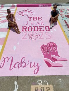 two women sitting on the ground in front of a pink sign that says the last rodeo