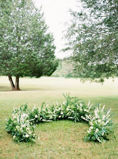 a circular arrangement of flowers and greenery in the middle of a grassy area with trees