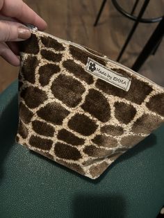 a giraffe print pouch sitting on top of a green chair next to a person's hand