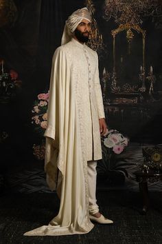 a man in a white outfit standing next to a wall with floral decorations on it