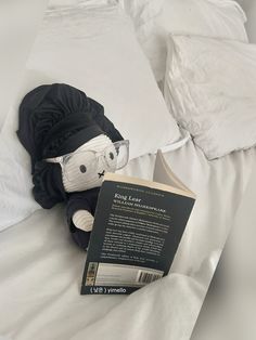 a stuffed animal is reading a book on a bed with white sheets and pillows in the background