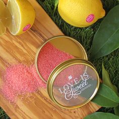 a wooden cutting board topped with two tins filled with pink glitter next to lemons