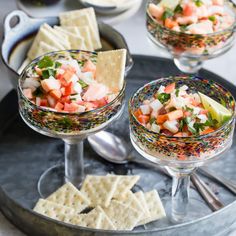 three glasses filled with fruit and crackers on a tray next to silver spoons