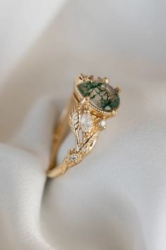 a gold ring with green and white stones on it sitting on a white satin surface