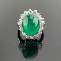 an emerald and diamond ring on a reflective surface