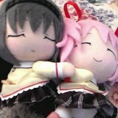 two dolls laying next to each other on top of a bed, one with pink hair