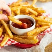 french fries with ketchup in a red basket on a white and red checkered tablecloth