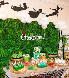 a table topped with cakes and desserts next to a wall covered in greenery