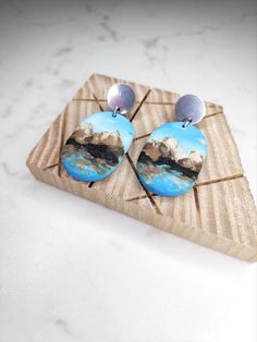 a pair of earrings with mountains in the background on a wooden stand, sitting on a marble surface