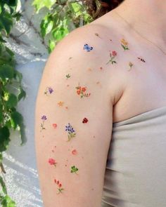 a woman with flowers painted on her arm and shoulder is standing in front of a tree