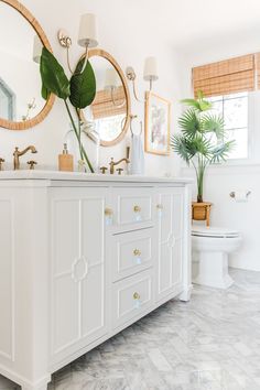 a white bathroom with two mirrors and a toilet in the corner next to a plant