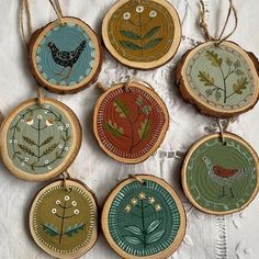 six wooden ornaments with birds and flowers are hanging on a white tablecloth covered surface