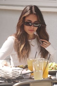 a woman wearing sunglasses sitting at a table with food and drinks in front of her